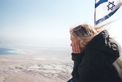 Young woman looks over a desert with flag of Israel behind her. 